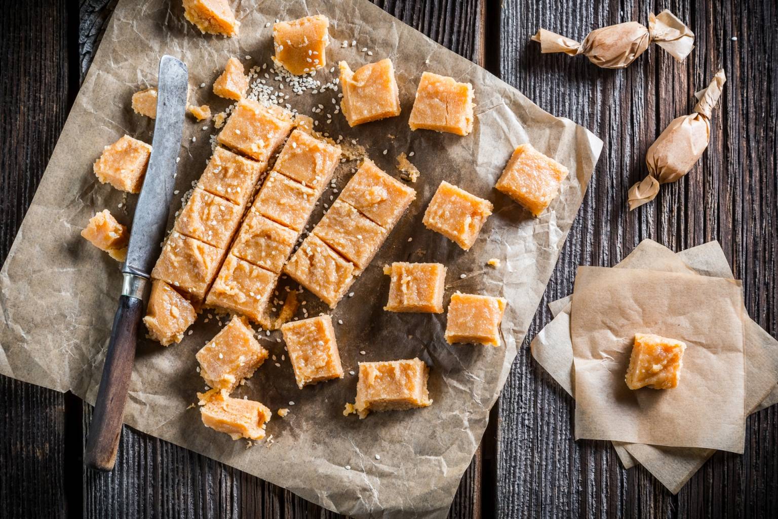 Jak leczyć cukrzycę typu 2? Na ciemnym drewnianym blacie, na papierze do pieczenia leżą pokrojone w kostkę domowe karmelowe cukierki. Obok leży długi nóż z drewnianą rękojeścią.