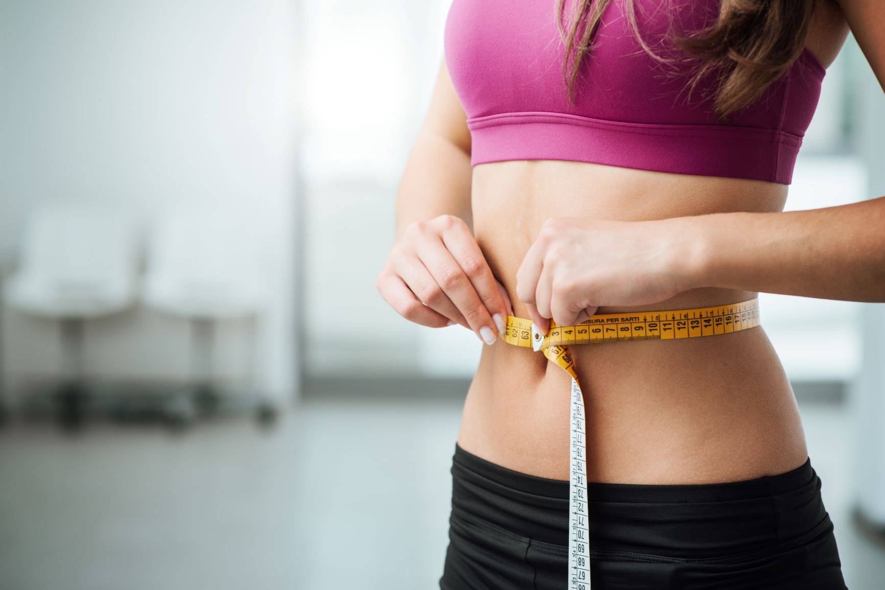 Dieta ośmiogodzinna - ile można schudnąć? Kobieta w stroju sportowym mierzy się w talii centymetrem.
