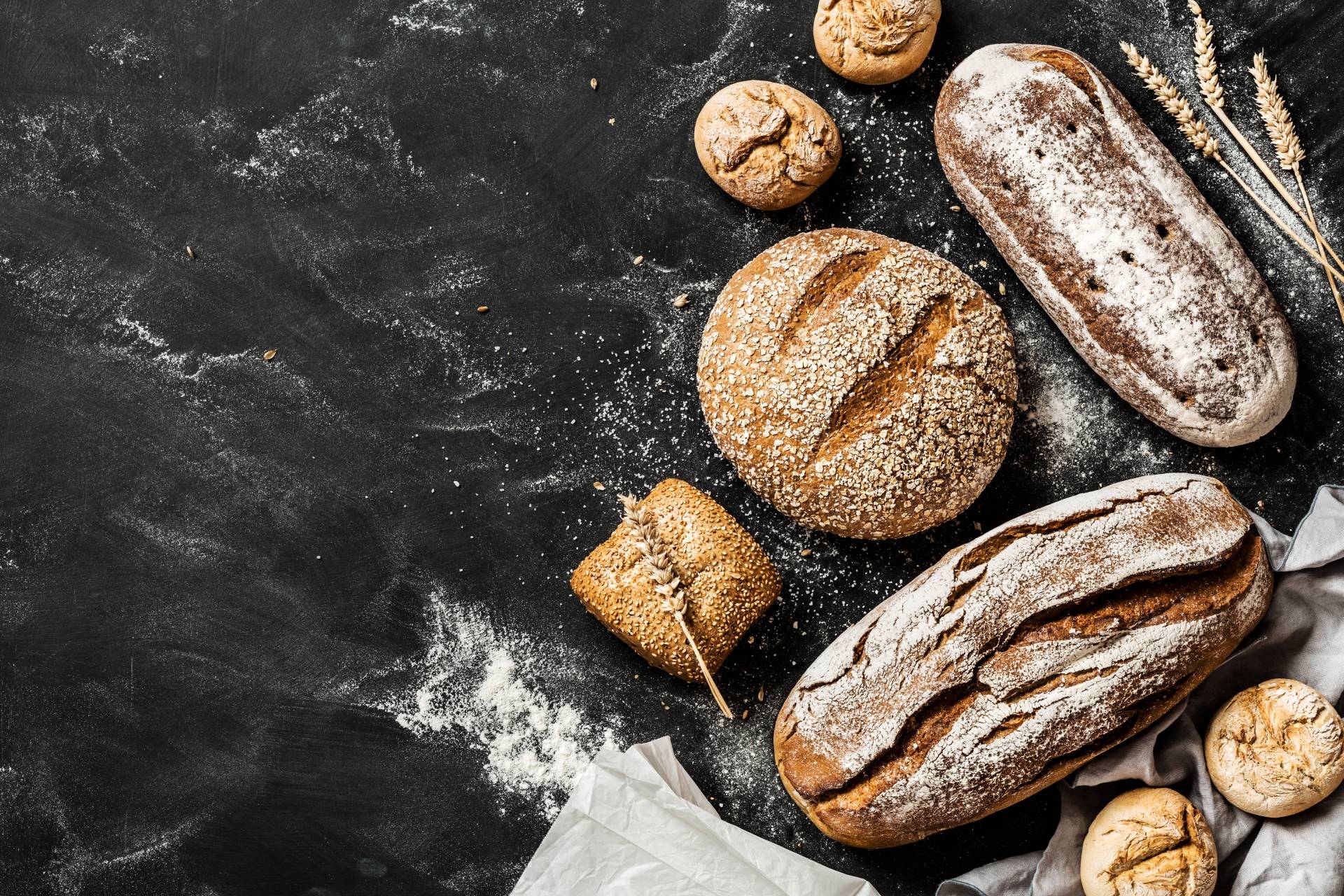 Dieta przeciwgrzybicza - wyeliminuj gluten. Bohenki świeżego chleba oprószone mąką na ciemnym tle.