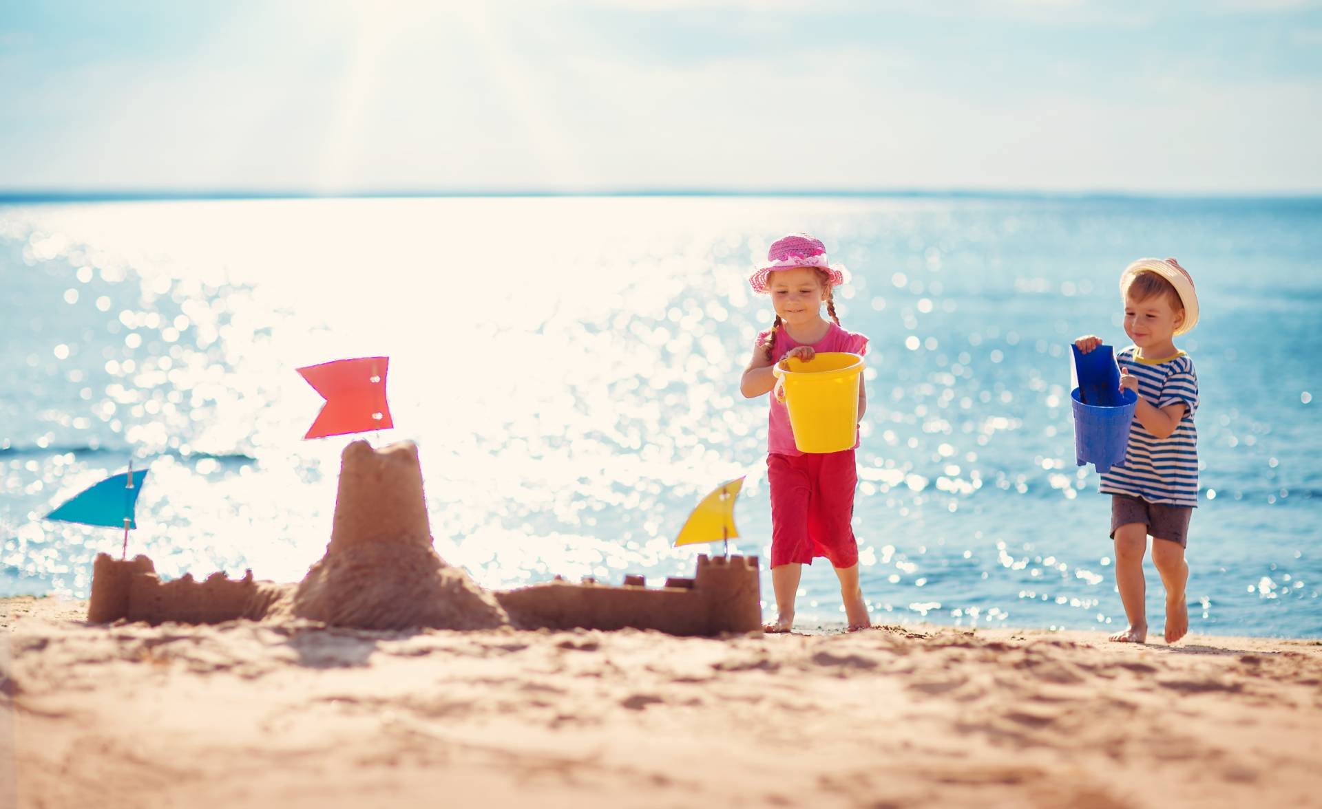 Dzieci budują zamek z piasku na plaży. Jak chronić dziecko przed upałem i udarem słonecznym?