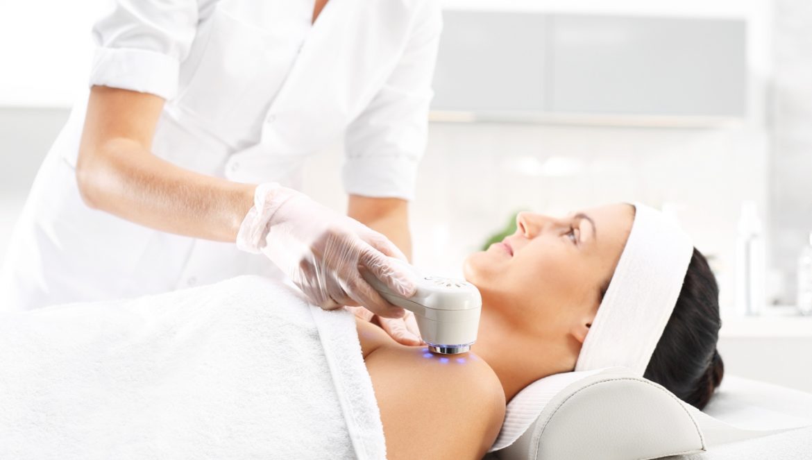 Fototerapia (światłoterapia) - na czym polega terapia światłem? Kobieta poddaje się zabiegowi kosmetycznemu z użyciem lampy do naświetlania w gabinecie kosmetycznym.