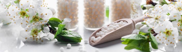 Ignatia amara - lek homeopatyczny w 3 fiolkach stoi na białym blacie obok białych kwiatów jabłoni.
