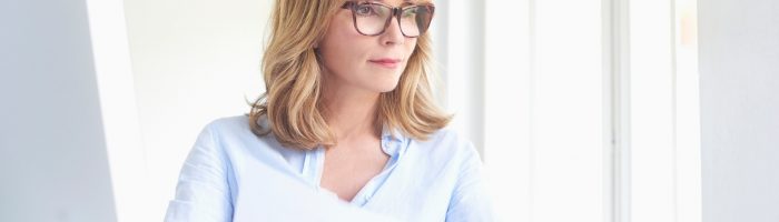 Jak dbać o wzrok po 40? Kobieta businesswoman w okularach z rogową oprawką siedzi przy komputerze.