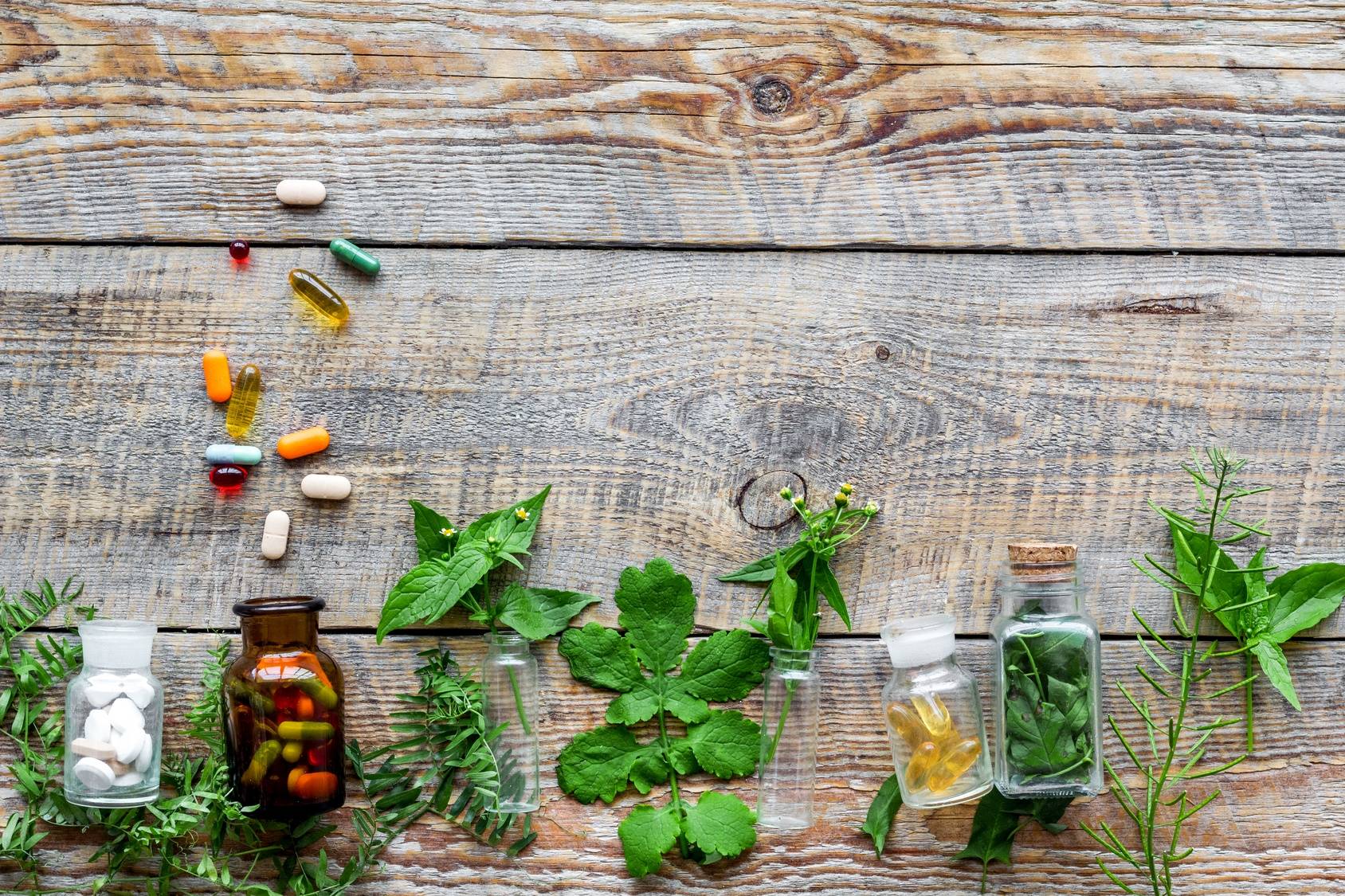 Leki homeopatyczne w fiolkach i zioła leżą na drewnianym blacie.. Calcarea carbonica.