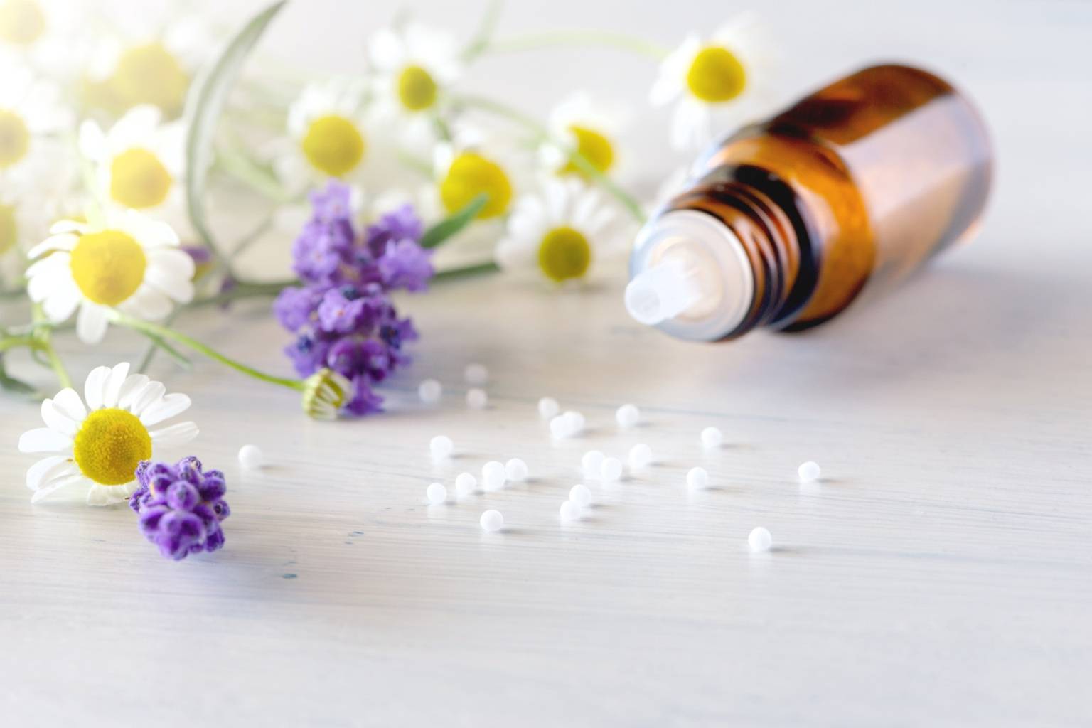 Leki homeopatyczne na dolegliwości w ciąży - granulki rozsypane z fiolki na blacie, obok leżą kwiaty rumianku.