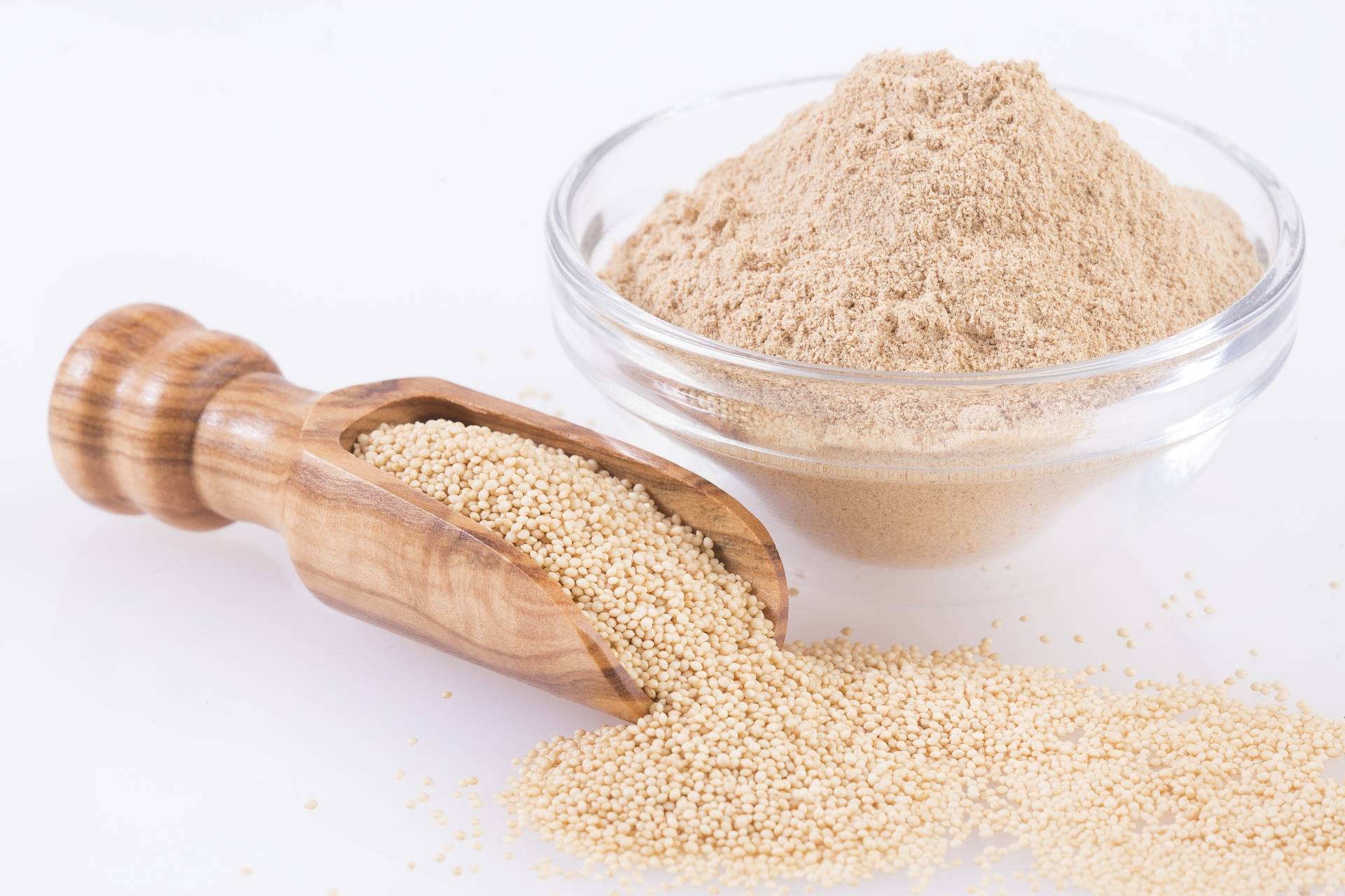 Mąka z amarantusa w szklanej miseczce i drewnianej łyżce na białym blacie. Mąka bez glutenu.