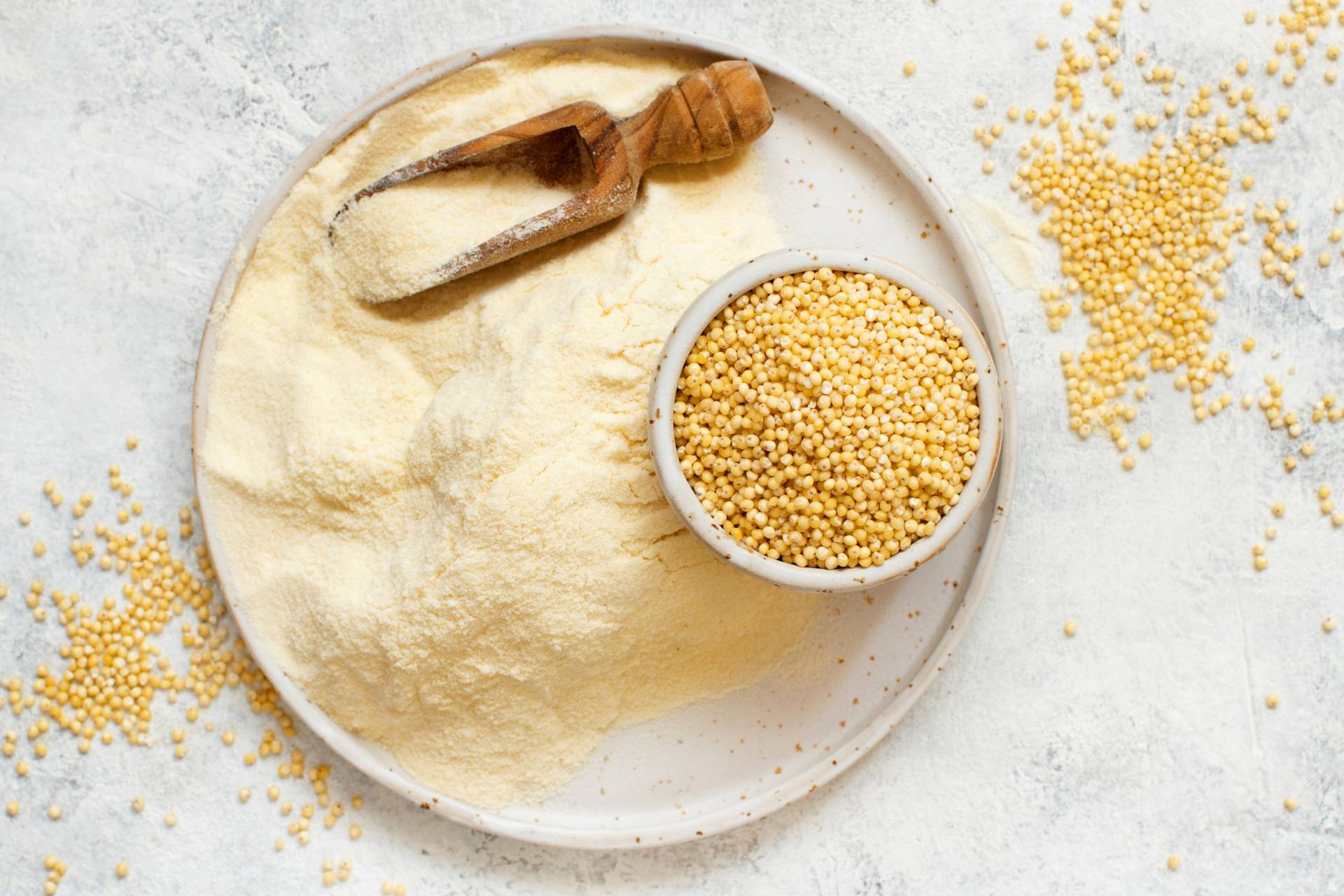 Mąka jaglana na białym talerzu, obok leży proso. Mąki bez glutenu.