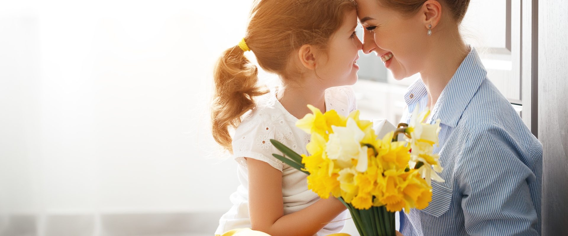 Mama i córka - szczególna relacja - wywiad z psycholożką Joanną Kot. Mama i córeczka przytulają się do siebie, trzymając w rękach bukiet żonkili.
