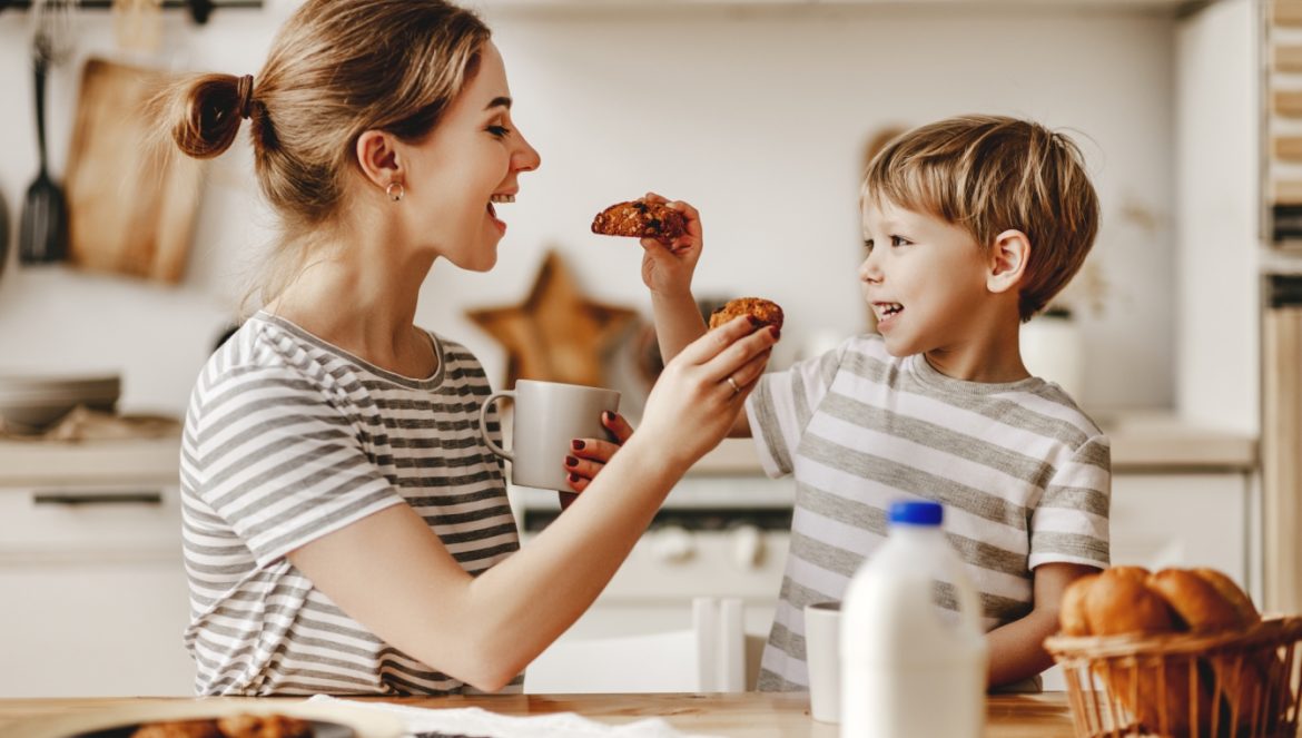 Dlaczego wspólne posiłki są ważne dla dzieci? Mama i synek częstują się nawzajem ciasteczkami, siedząc przy stole w kuchni.