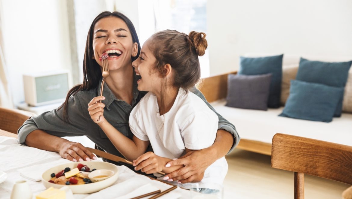 Rozgrzewające potrawy i napoje - 8 przepisów na rozgrzewające dania. Mama z córką śmieją się przy śniadaniu w domowej kuchni.