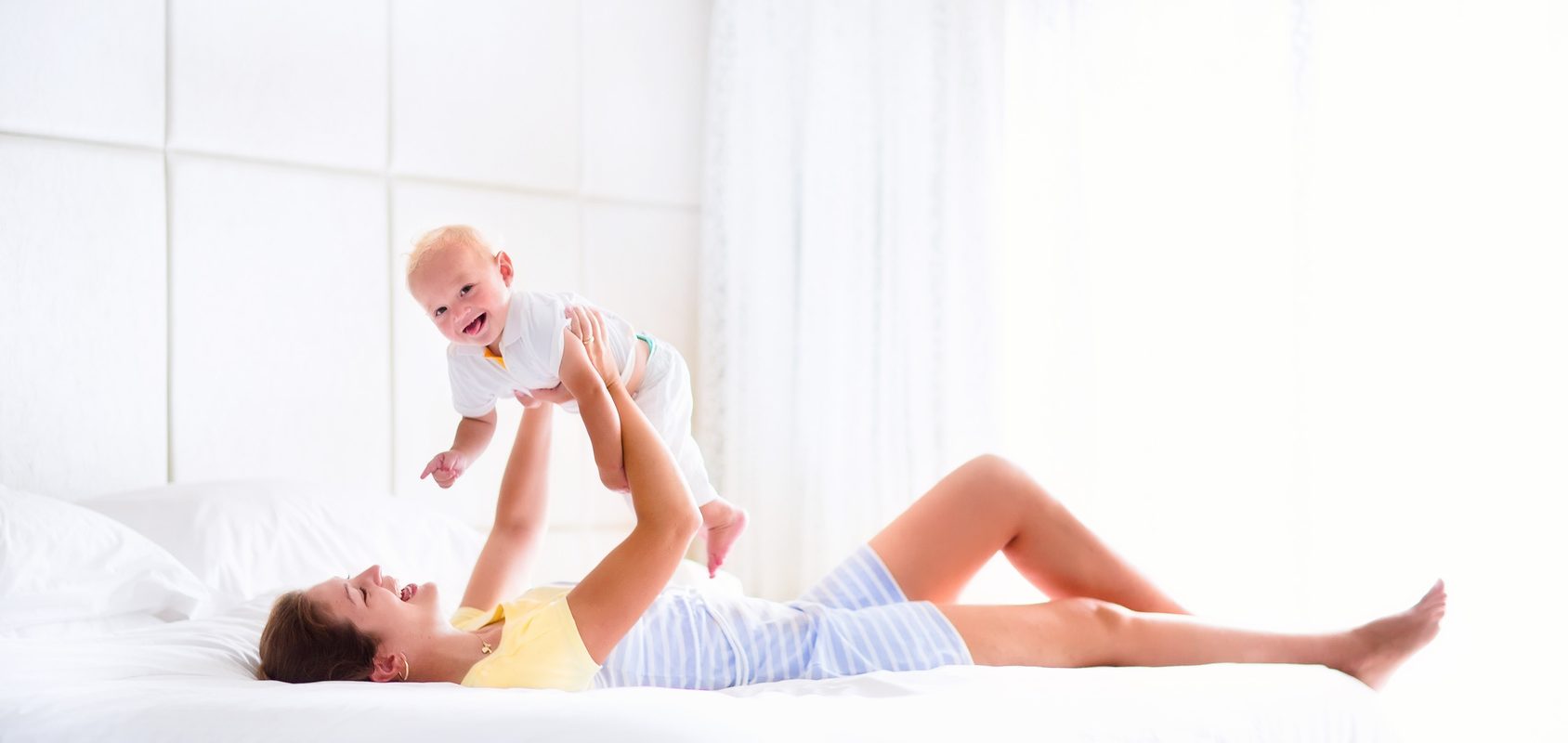 Blizna po cesarce - jaki ma wpływ na zdrowie? Mama leży na łóżku i podnosi do góry niemowlę.