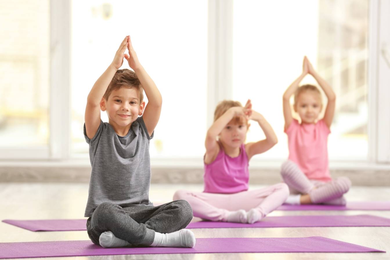 Mindfulness dla dzieci - na czym polegają treningi uważności dla maluchów i nastolatków? Przedszkolaki siedzą na matach w sali gimnastycznej i trenują jogę i medytację.