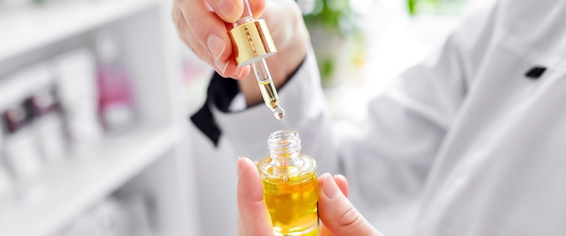 Olejek arganowy w pielęgnacji. Farmaceutka lub kosmetolog trzyma w ręku otwartą buteleczkę z olejkiem i podnosi pipetę do góry.