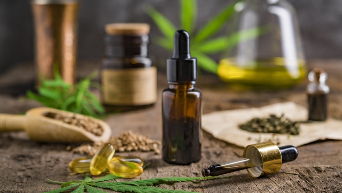 Olejek CBD - czym jest i jak go stosować? Co warto wiedzieć o oleju z konopi leczniczej? Fiolka z olejkiem na drewnianym tle.
