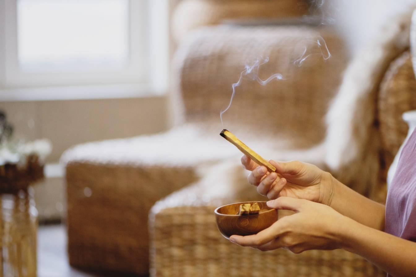 Palo santo i biała szałwia nie są ani zdrowe ani eko! Czego użyć zamiast? Kobiece dłonie okadzają salon domowy kadzidełkiem.