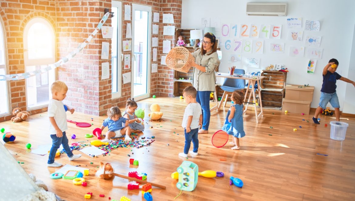 Adaptacja w przedszkolu - jak pomóc dziecku zaaklimatyzować się w nowym miejscu? Pani wychowawczyli bawi się z przedszkolakami w sali zabaw w przedszkolu.