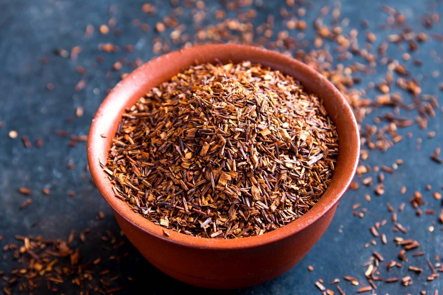 Susz czerwonej herbaty rooibos w miseczce na niebieskim blacie. Jakie właściwości ma rooibos?