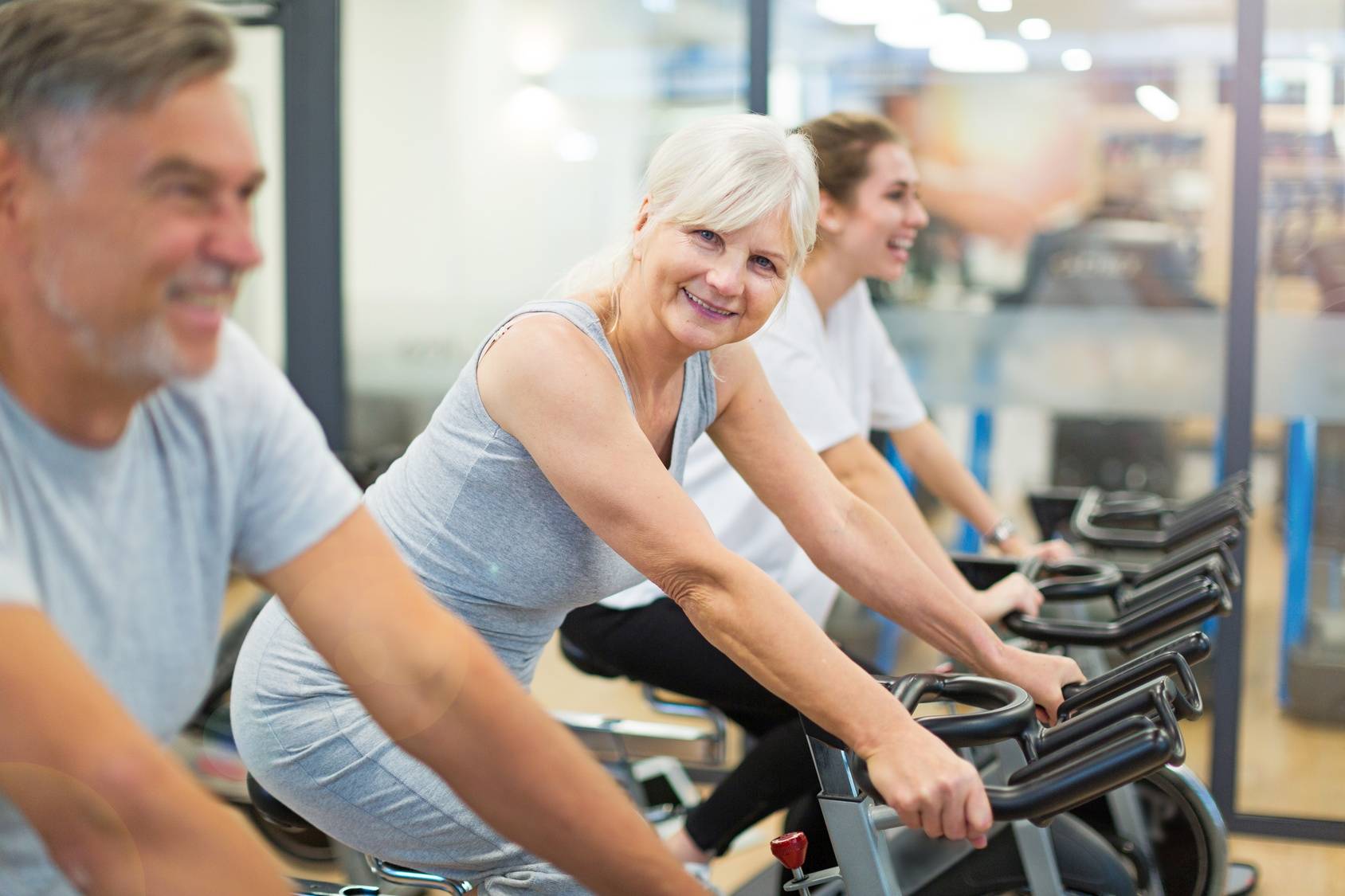 Trening na siłowni dla seniorów. Kobieta i mężczyzna w starszym wieku ćwiczą na rowerku na siłowni.