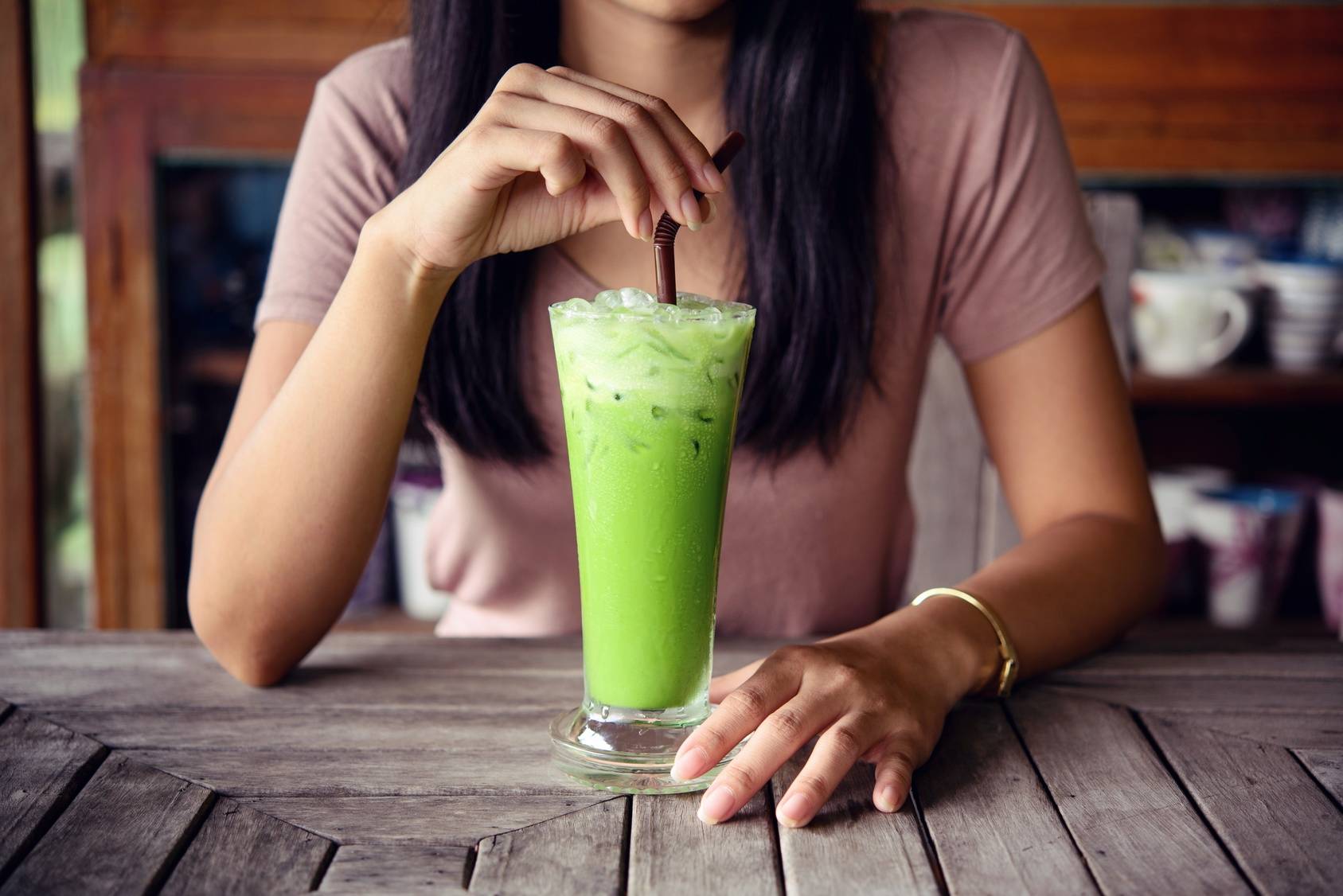 Dlaczego warto pić matchę? Kobieta pije smoothie z matchą z wysokiej szklanki.