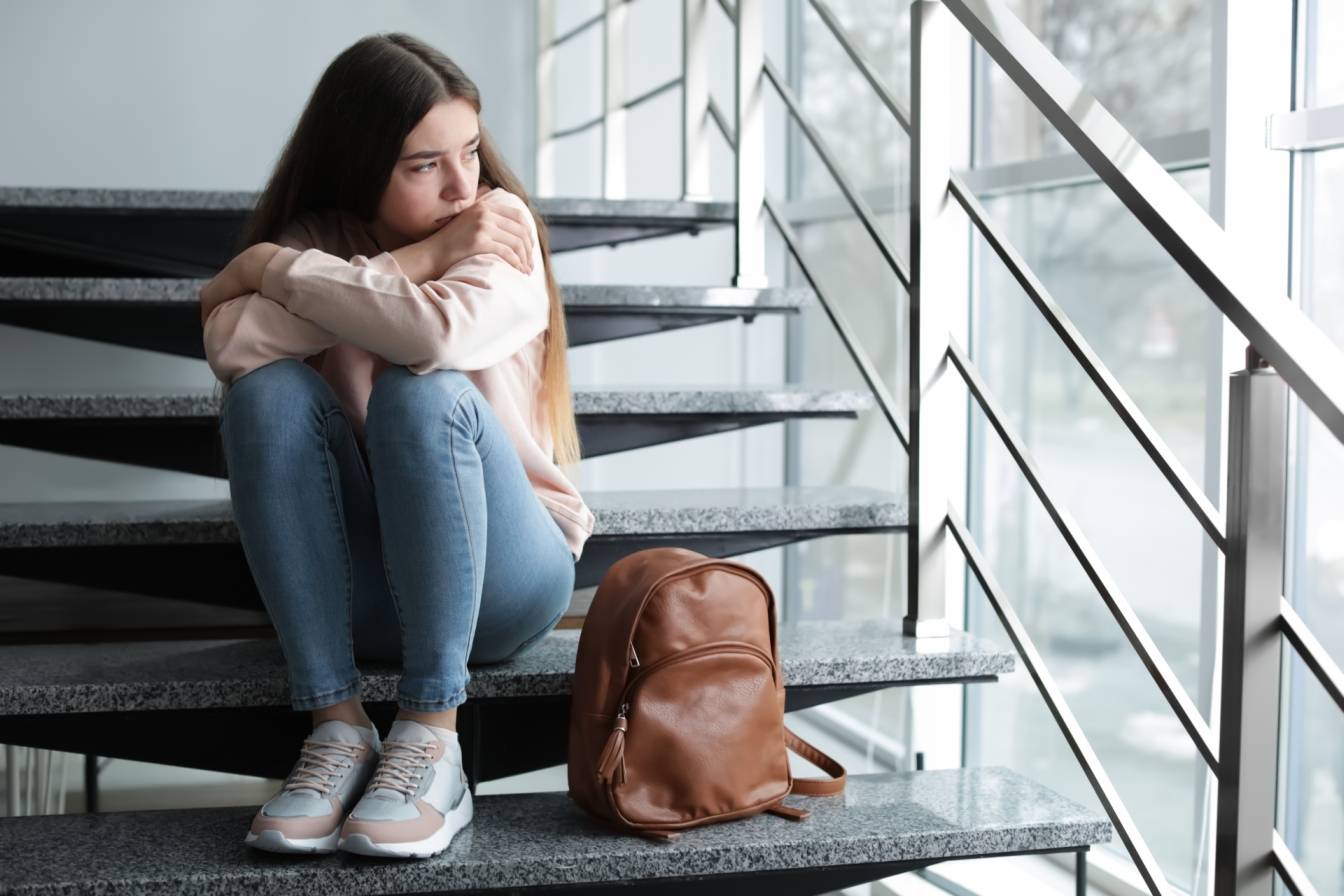Jak pomóc dzieciom z problemami depresyjnymi i lękowymi? Smutna nastolatka siedzi na schodach na klatce schodowej.