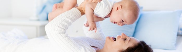 Jak zadbać o siebie po porodzie według wskazówek tradycyjnej medycyny chińskiej? Mama bawi się z niemowlęciem na łóżku.