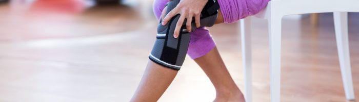 Jak złagodzić ból po urazie lekami homeopatycznymi? Co na urazy i stłuczenia? Kobieta trzyma się za bolące kolano w trakcie rehabilitacji.