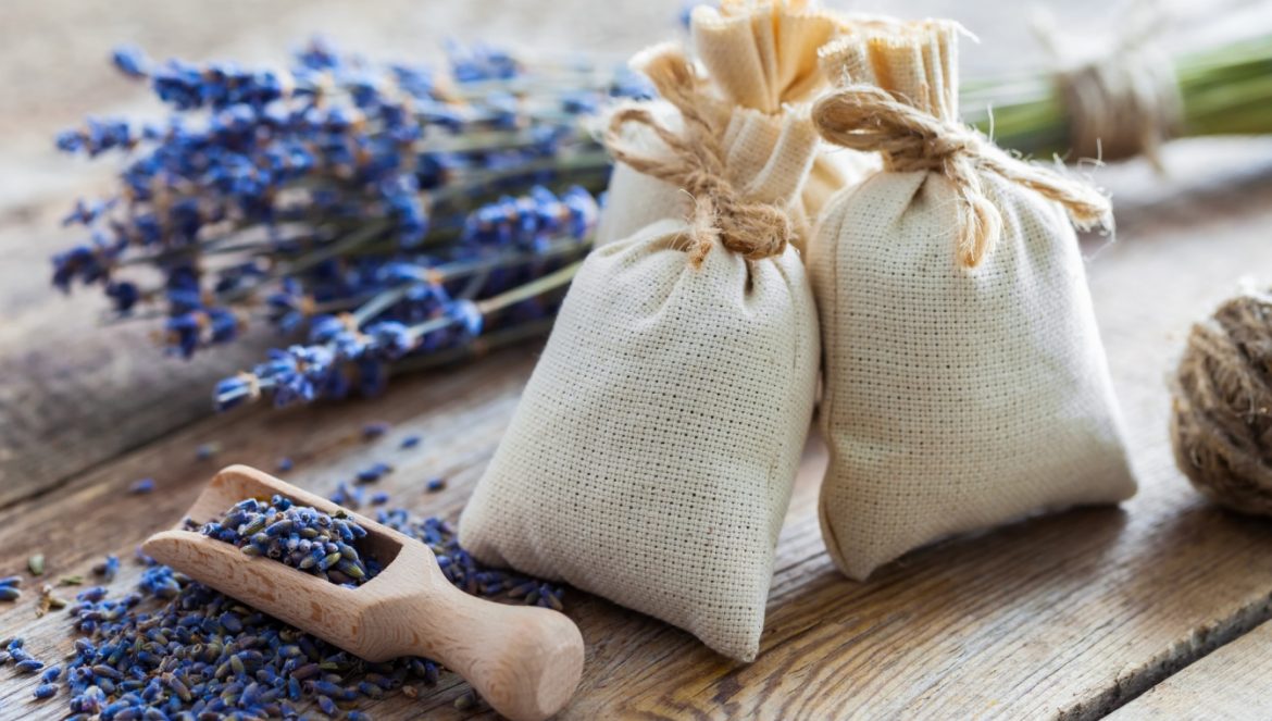 Co zrobić z lawendy? 6 lawendowych inspiracji DIY: woreczki na mole, herbata, syrop i nalewka lawendowa, sól do kąpieli i hydrolat. Dwa lniane woreczki na mole z lawendą na drewnianej podłodze, obok leżą ususzone gałązki lawendy.