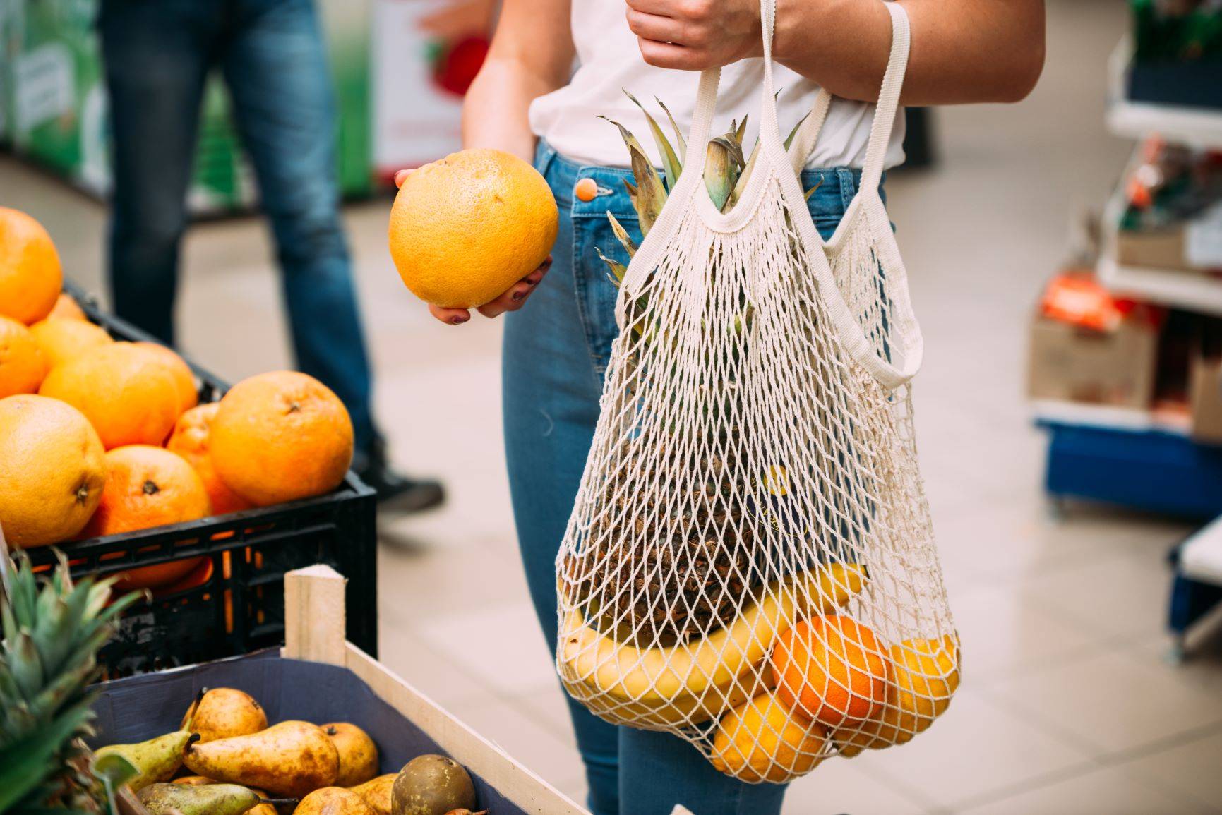 Jak być eko? Jak zacząć żyć ekologicznie w duchu zero waste? Kobieta robi zakupy na targu i wkłada owoce do ażurowej torby ekologicznej.
